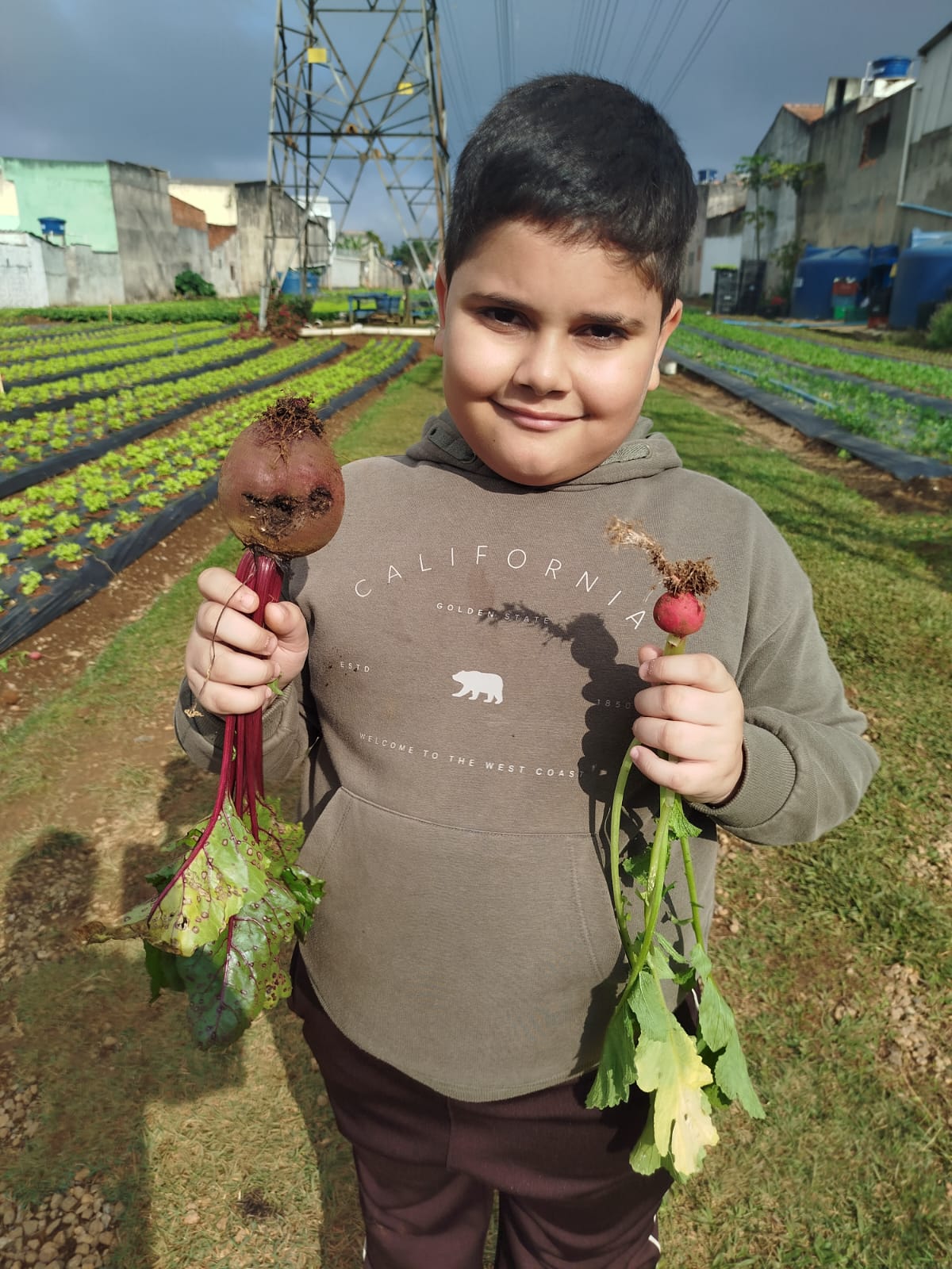 Criança exibindo beterraba e rabanete colhidos em horta escolar